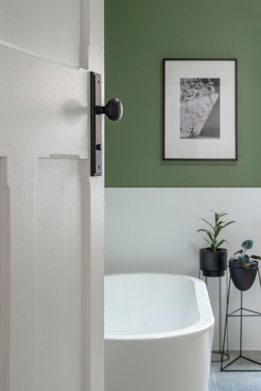 White 3 panel door with a black door knob leading into a bathroom with a freestanding bath and green wall