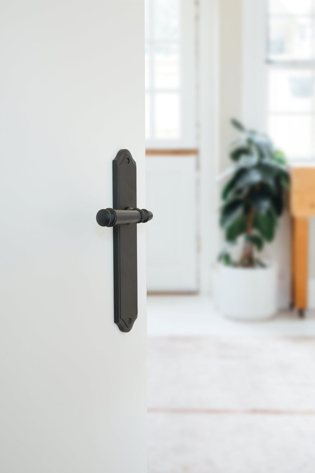 Lever door handle on long shouldered backplate in bronze finish pictured on a white door.