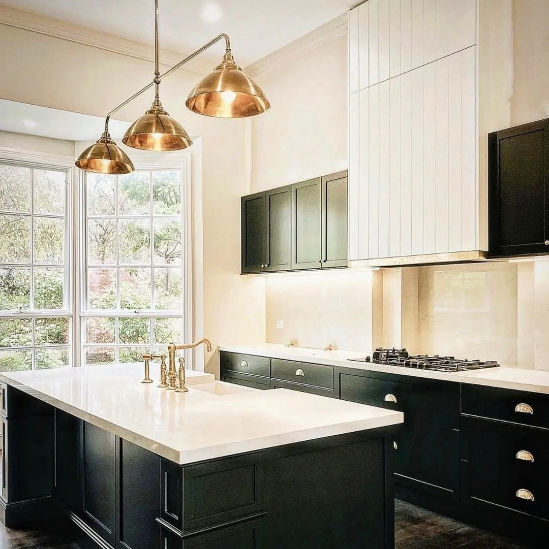 Modern kitchen with black island and white countertops, featuring brass fixtures and pendant lights.