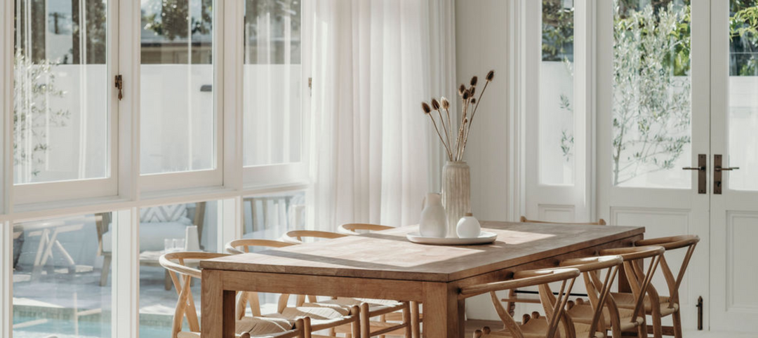 Sunlit dining room with a timber dining table and chairs, white French doors and casement windows with antique brass hardware.