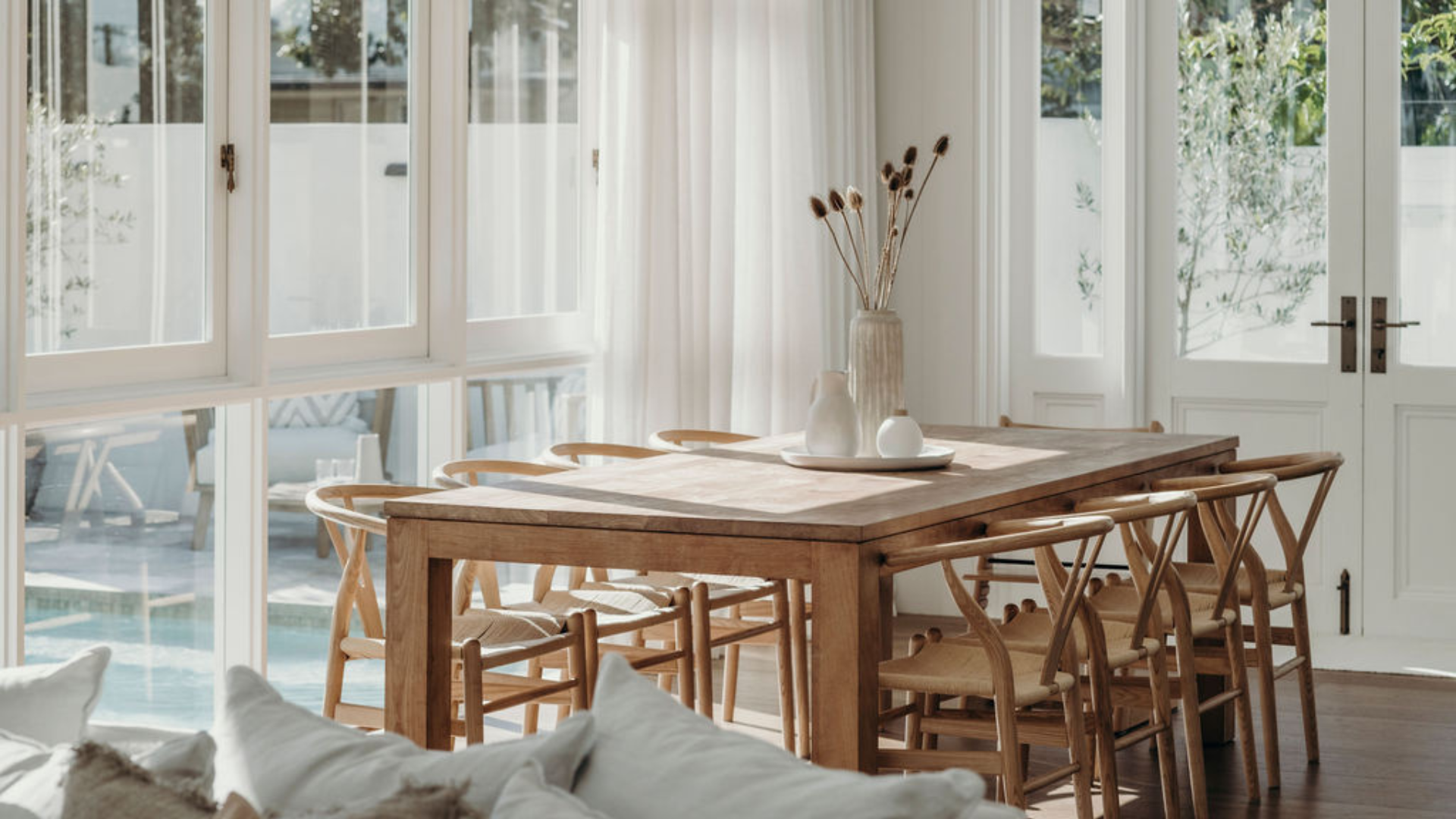 Sunlit dining room with a timber dining table and chairs, white French doors and casement windows with antique brass hardware.